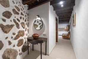 A hallway with a stone wall, a wooden table with a vase, a mirror, and a chair.