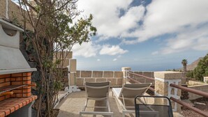 Eine Terrasss mit Grill, zwei Stühlen und Meerblick.