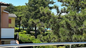 A residential area with a yellow building, a balcony, and surrounding greenery including pine trees. - Great and bright flat with pool (Bibione)