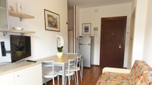 Un espacio habitable compacto con comedor, sofá, televisor y refrigerador.