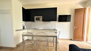 Een moderne keuken met een magnetron, spoelbak en een eethoek met transparante stoelen en een tafel.