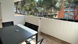 A balcony with a table and chairs, overlooking a residential area with trees and buildings. - Stylish Bibione flat with pool access (Bibione)
