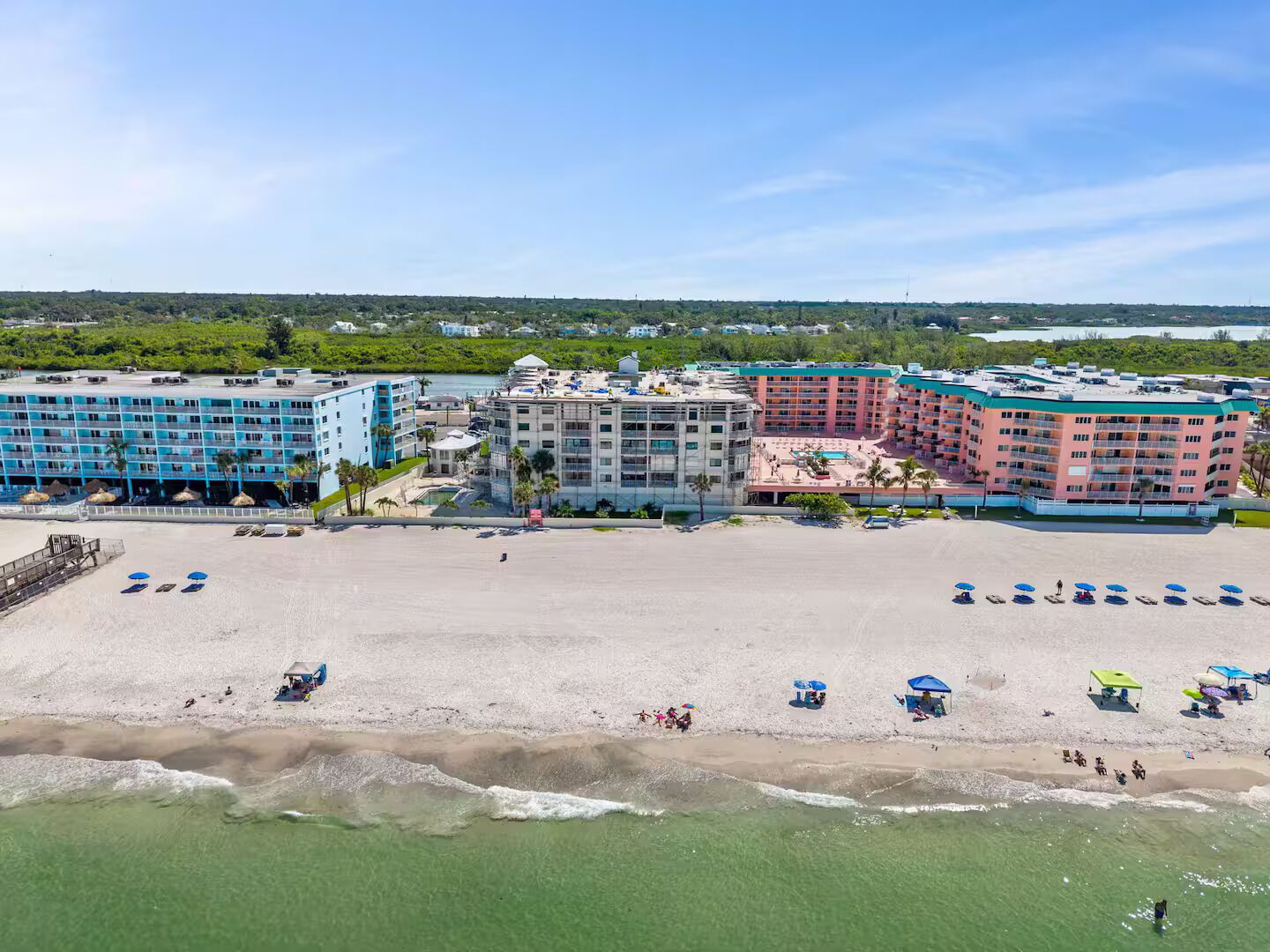 Ein Hotel direkt am Strand mit mehreren Gebäuden, einem Sandstrand und blauem Himmel.