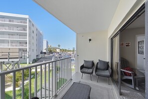 A balcony with two chairs, a view of a parking lot, and a building with balconies.