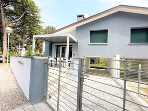 Une maison moderne dotée d’un patio couvert, d’une entrée sécurisée par un portail et offrant une vue sur un jardin.