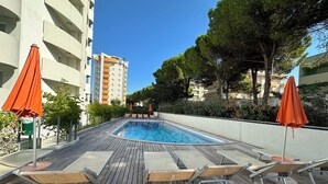 Ett poolområde med trädeck, solstolar och orangea parasoller.