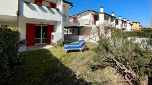 A modern residential building with a red and white facade, balconies, and a small garden area with a blue lounge chair.
