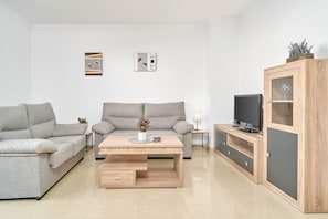 Ein modernes Wohnzimmer mit zwei grauen Sofas, einem Holztisch, einem Fernseher auf einer Holzkommode und zwei an der Wand hängenden Kunstwerken.