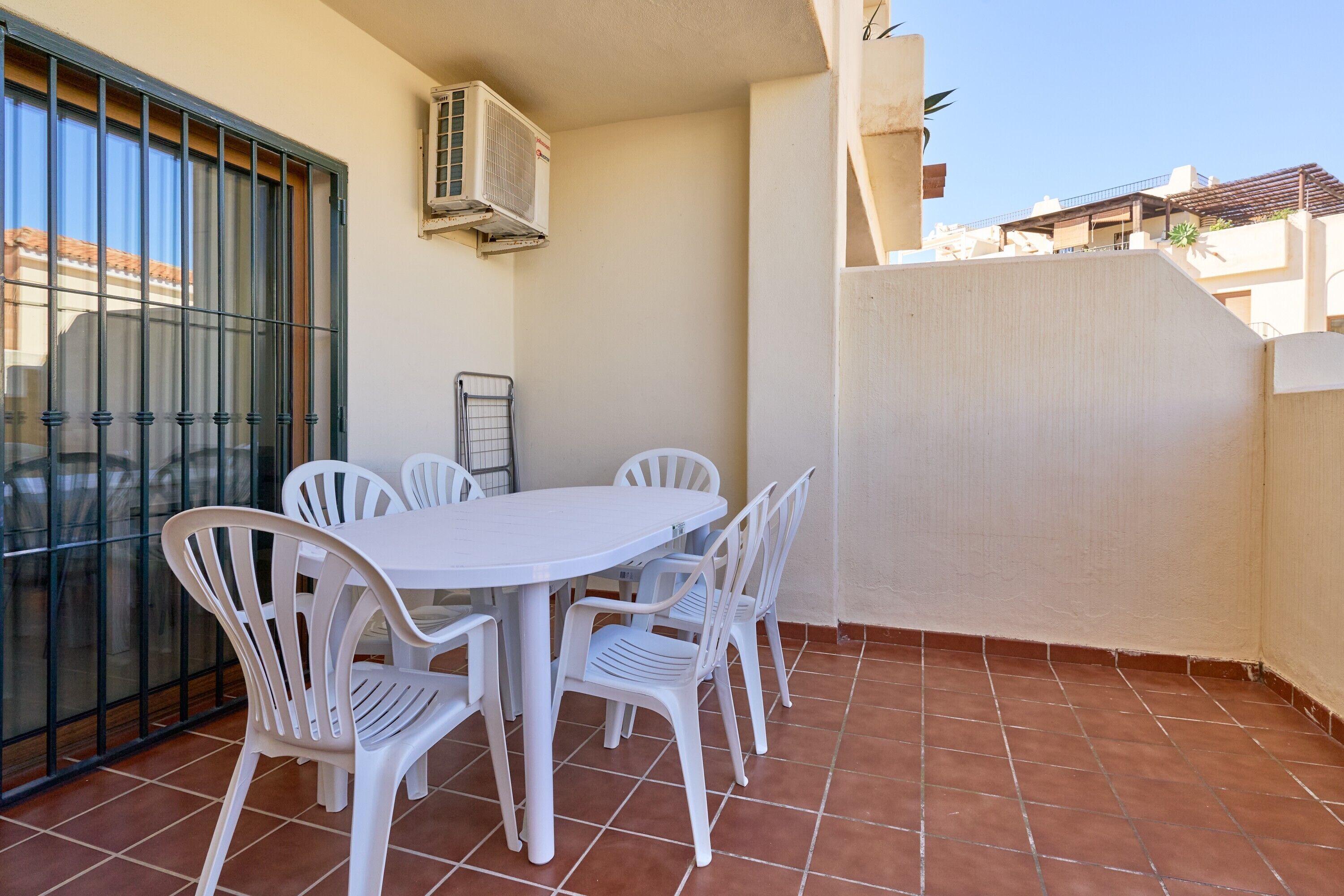 A patio with a white table and chairs, an air conditioning unit, and a view of neighboring buildings.