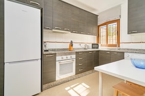 Eine moderne Küche mit dunklen Schränken, einem weißen Kühlschrank, einem Herd und einer Mikrowelle.