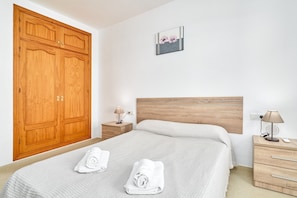 Ein Schlafzimmer mit einem großen Holzschrank, einem Bett mit weißer Bettdecke, zwei Nachttischen mit Lampen und einem kleinen Wandbild.