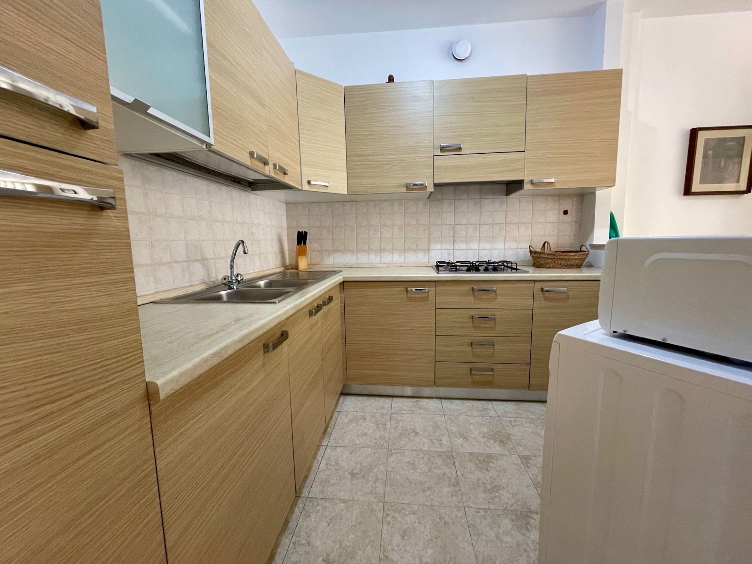 A compact kitchen with wooden cabinets, a stainless steel sink, a gas stove, and a built-in microwave.