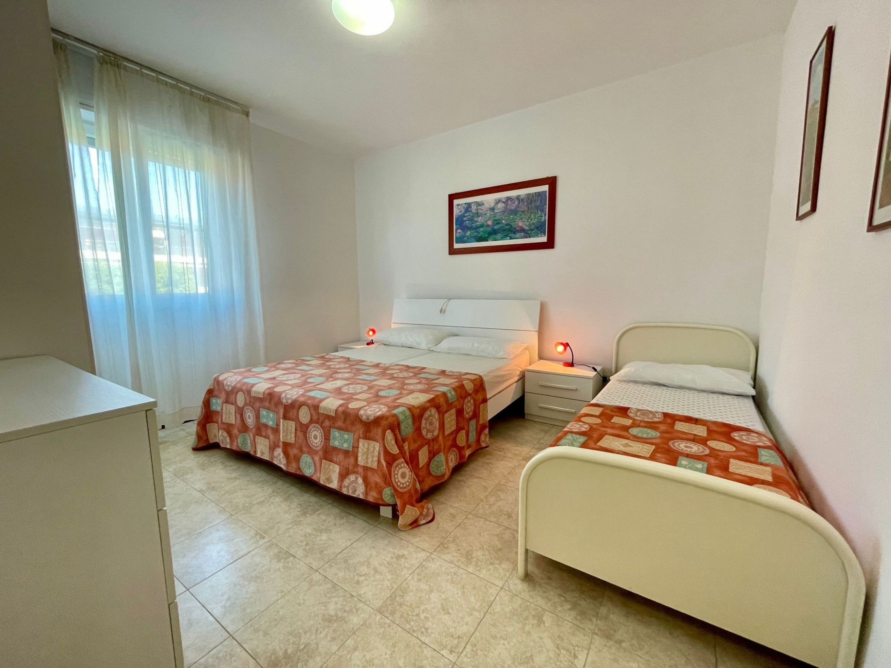 Quarto com duas camas, uma escrivaninha e uma janela com cortinas.