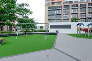 Ein Spielplatz mit Schaukeln und Rutschen, einem grünen Rasenplatz und einem Gebäude mit mehreren Fenstern im Hintergrund.