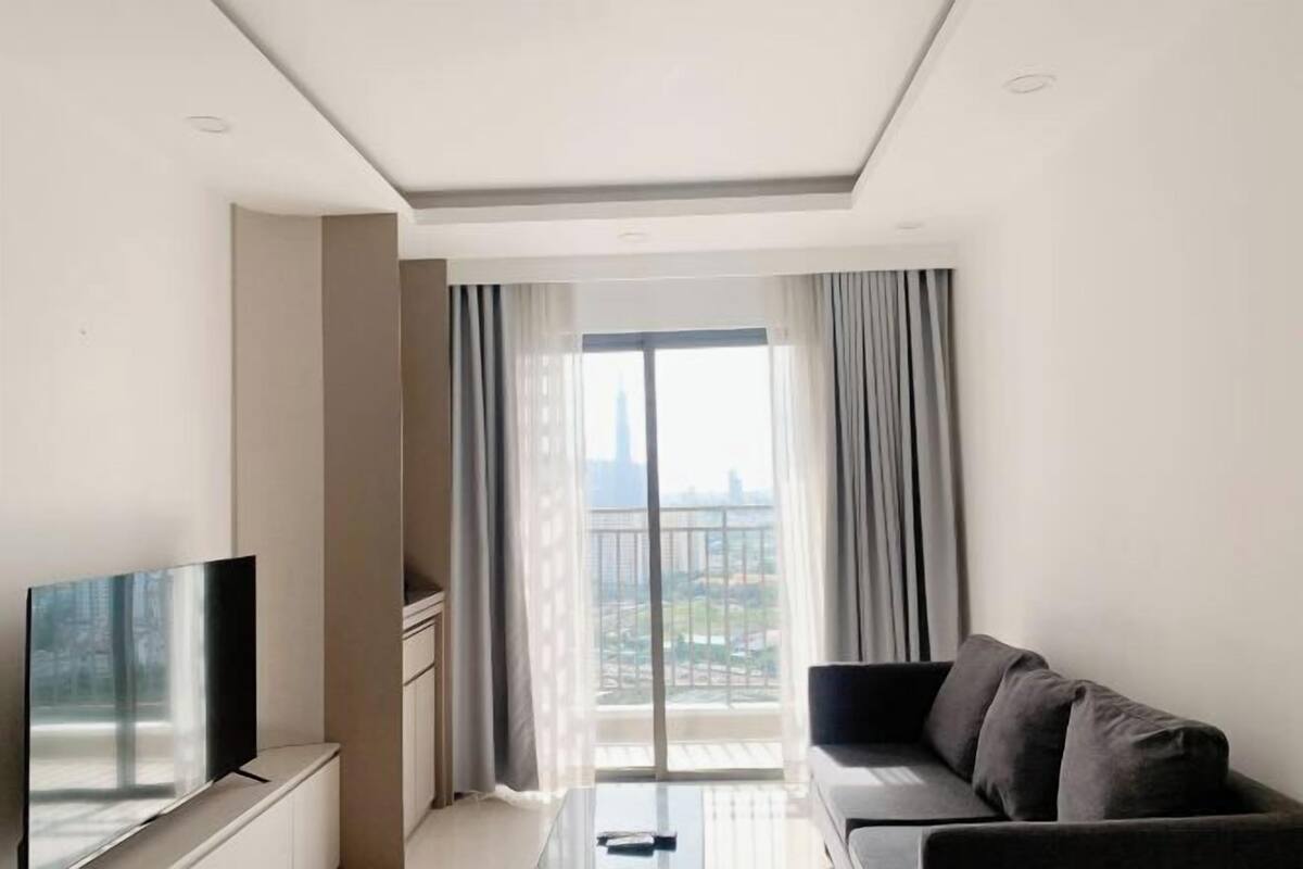 Ein modernes Wohnzimmer mit Flachbildfernseher, einer Couch, einem Glastisch und einem großen Fenster mit Vorhängen.