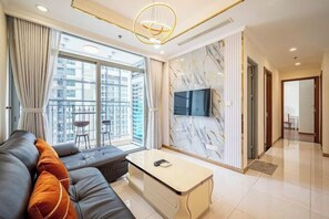 Ein modernes Wohnzimmer mit einer Couch, einem Couchtisch, einem Fernseher und einem Balkon mit Blick auf hohe Gebäude.