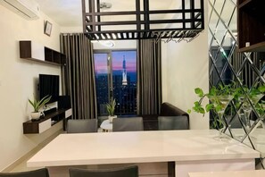 Ein moderner Essbereich mit einem weißen Tisch, dunklen Stühlen, einem Fernseher und Blick auf die Stadt.