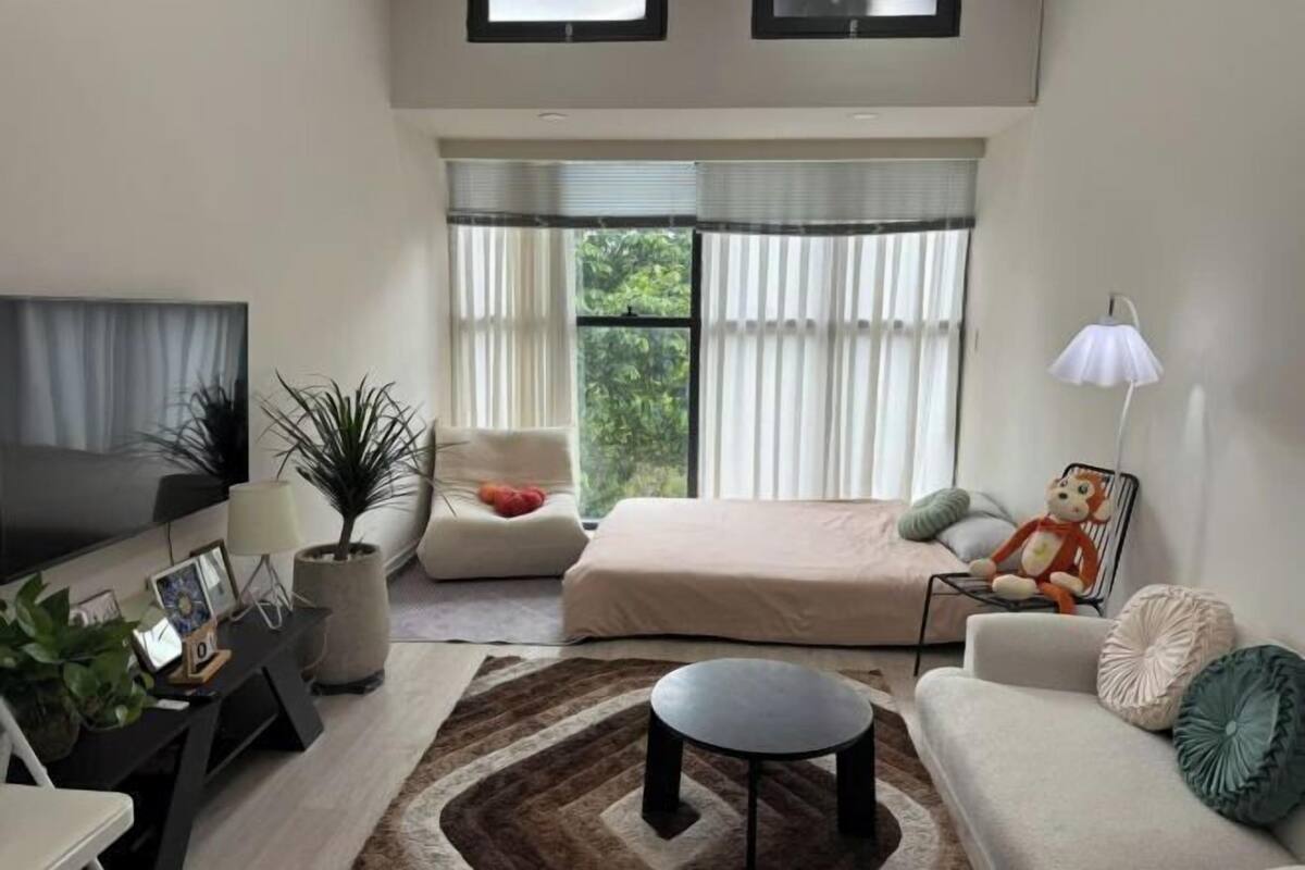 Ein modernes Wohnzimmer mit Sofa, Couchtisch, Fernseher, Lampe und einem großen Fenster mit Jalousien.