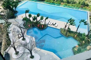 Piscina com design moderno, cercada por palmeiras e espreguiçadeiras.