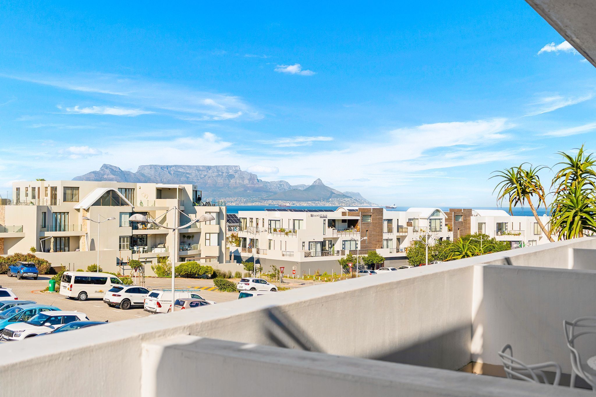 A coastal hotel with multiple buildings, a parking area, and a view of the sea and mountains.