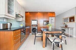 Une cuisine moderne avec des meubles en bois, des appareils en acier inoxydable et un coin repas comprenant une table et des chaises.