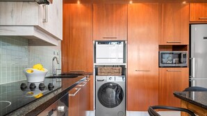A compact kitchen with a built-in washer and dryer, a microwave, and a sink with a modern faucet. - Eden On The Bay 104 (Cape Town)