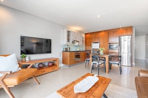 A modern kitchen with wooden cabinets, a stainless steel refrigerator, and a dining area with a table and chairs.