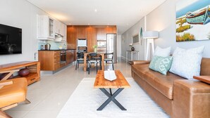 A modern living room with a brown leather sofa, a wooden coffee table, and a TV mounted on the wall. - Eden On The Bay 104 (Cape Town)