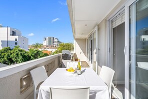 A balcony with a table set for two, a bottle of wine, and a bowl of fruit.