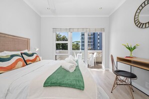 A modern hotel room with a large bed, a desk, and a view of the city.