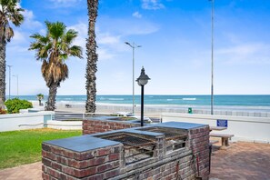 A patio area with a brick barbecue grill, a street lamp, and a view of the beach and ocean. - 14 Cap D'azur (Cape Town)