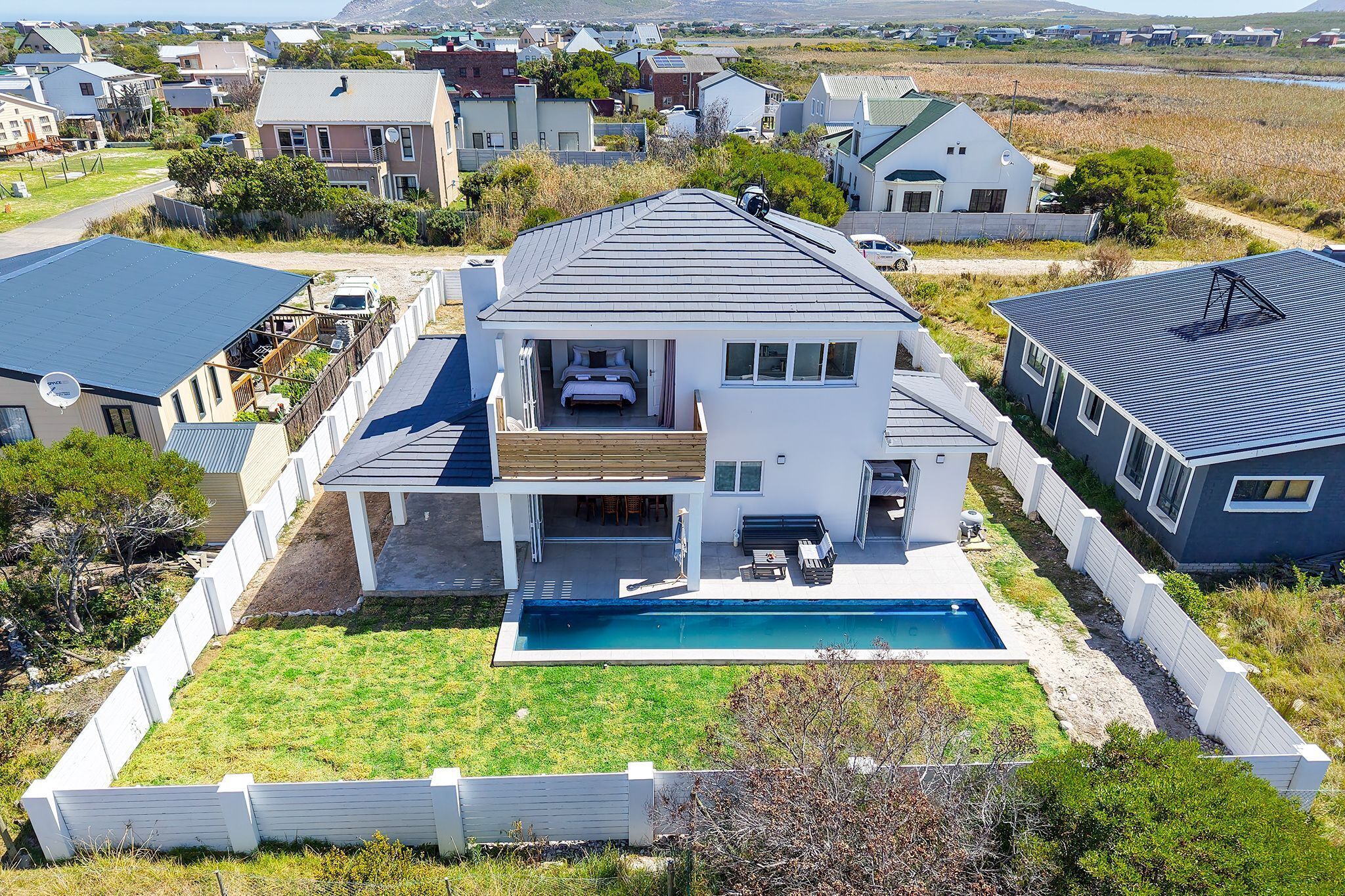 Une maison à deux étages avec une piscine, entourée d’une clôture blanche et d’une cour verdoyante.