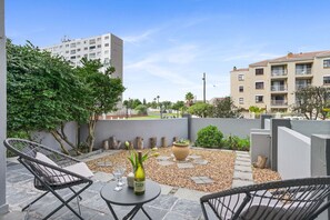 A rooftop patio with outdoor seating, a table with a bottle and glass, and a view of surrounding buildings. - The Sands BG3 (Cape Town)