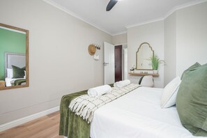 Une chambre d’hôtel avec un lit, un miroir, une porte et une petite étagère sur laquelle se trouve une plante.