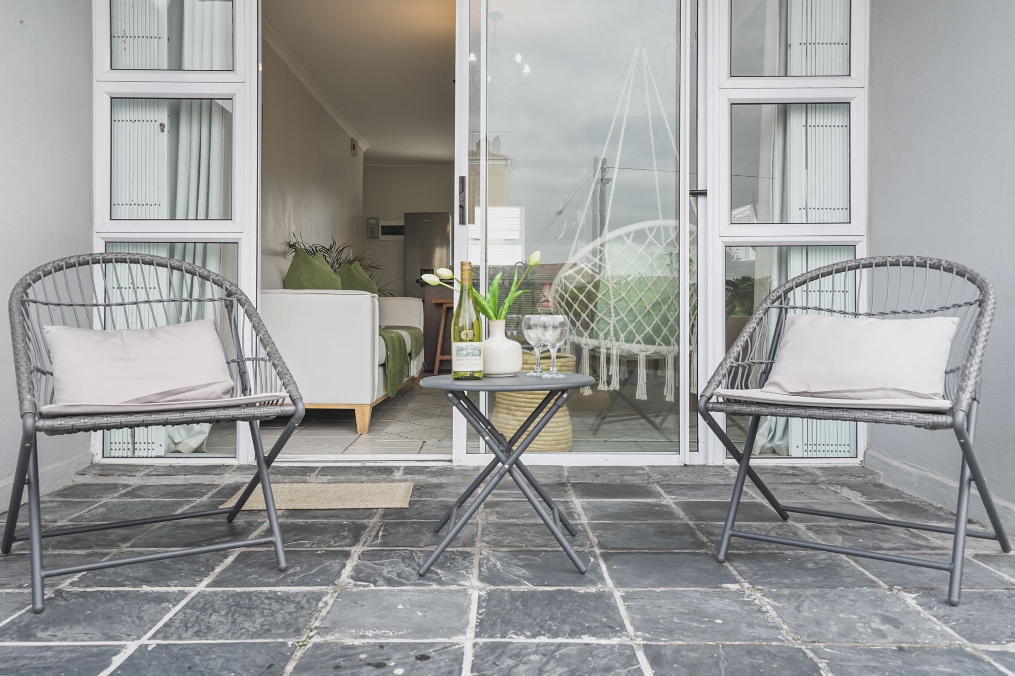 A balcony with two wicker chairs, a small round table, and a glass door leading to an interior space.