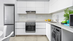 A modern kitchen with white cabinetry, a stainless steel refrigerator, an oven, a dishwasher, and a sink. - Beach Break 47 (Cape Town)