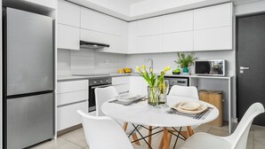 A modern kitchen with white cabinetry, a stainless steel refrigerator, and a dining area with a white table set for two. - Beach Break 47 (Cape Town)