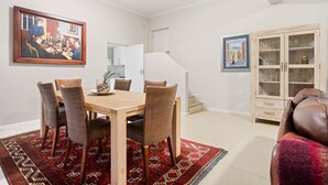 A dining area with a wooden table and wicker chairs, a red patterned rug, and a cabinet with glass doors. - Suikerbossie 52 (Cape Town)
