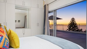 A bedroom with a large bed, white cabinets, and a balcony with a view of the sunset and a tree. - Suikerbossie 52 (Cape Town)
