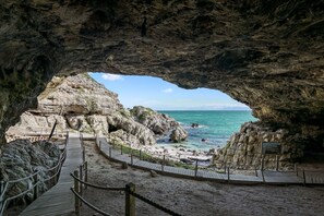 A cave entrance leading to a beach with a wooden walkway and a viewing platform. - The Tides at Gansbaai (De Kelders)