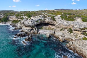 A coastal landscape with rocky cliffs, clear turquoise waters, and a paved path. - The Tides at Gansbaai (De Kelders)
