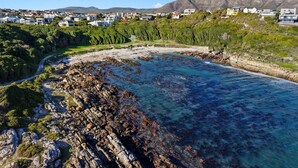 A coastal town with a rocky shoreline, clear blue waters, and residential buildings on a hillside.