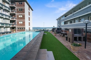 A swimming pool with a view of the sea, a grassy area, and a barbecue setup. - Searenity Tides (Cape Town)
