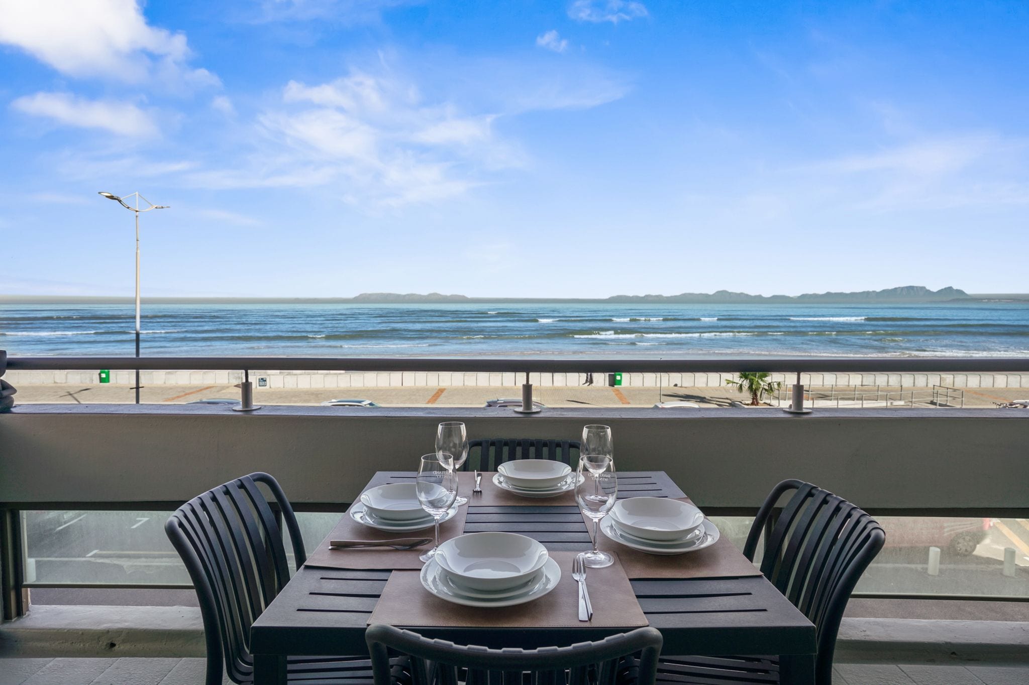 A table set for dining with a view of the ocean and beach.