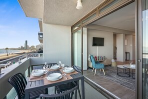 A balcony with a dining table set for four, overlooking a beach and city skyline. - Searenity Tides (Cape Town)