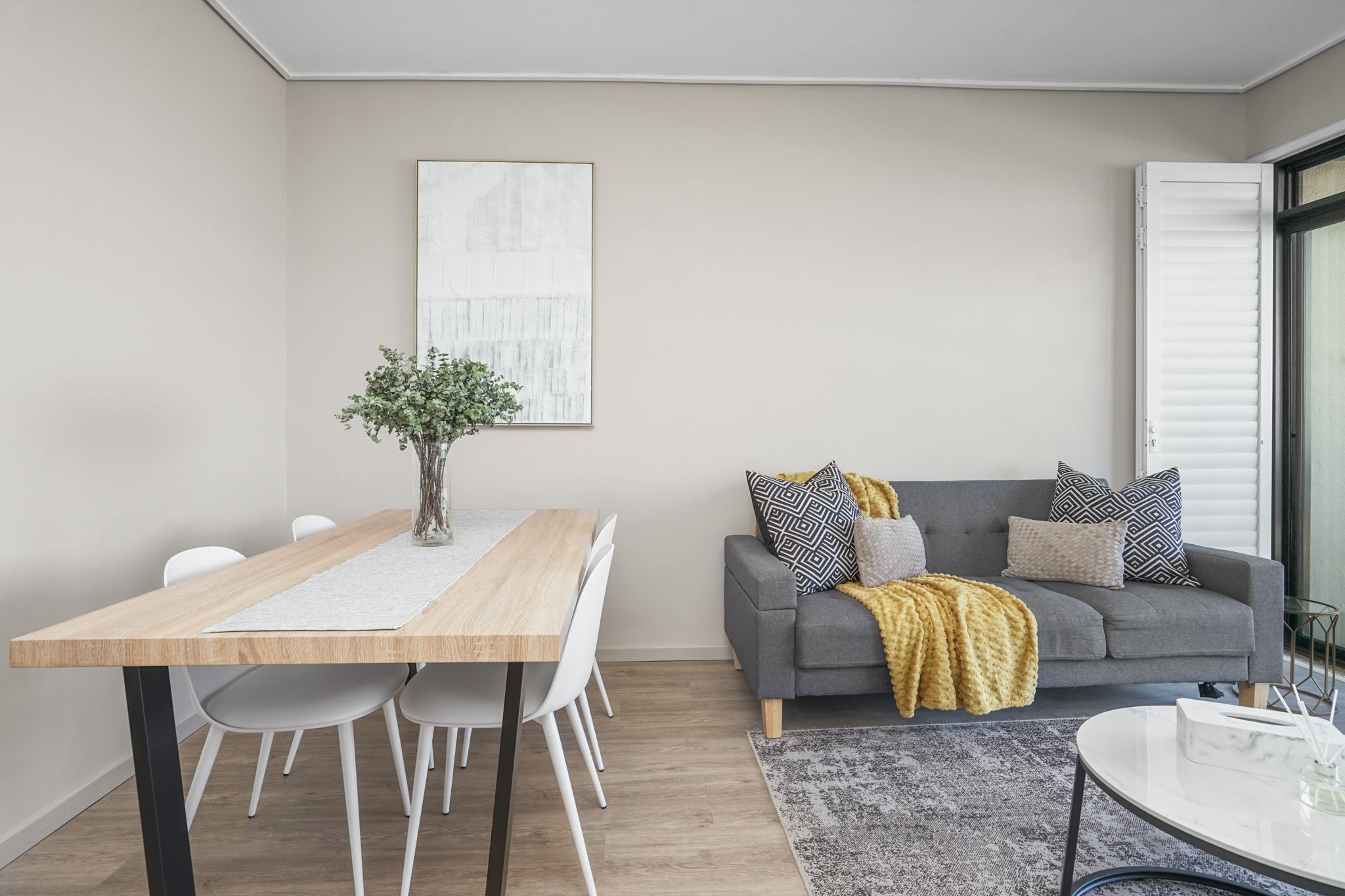 Una sala moderna con un sofá gris, una mesa de comedor de madera y una alfombra gris.
