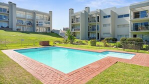 A modern apartment building with a swimming pool, green lawns, and a clear blue sky. - Balmoral Heights 20 (Cape Town)