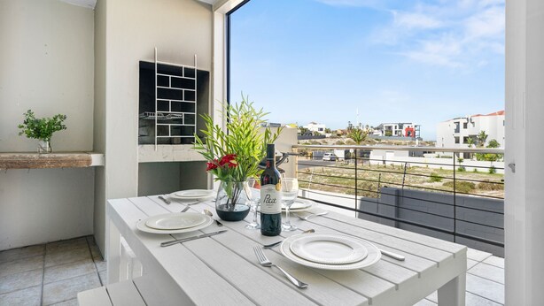 A balcony with a table set for dining, a bottle of wine, and a vase with flowers. - Balmoral Heights 20 (Cape Town)