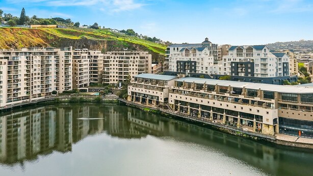 A modern hotel complex with multiple buildings, a central courtyard, and a river reflecting the architecture. - The Tygervalley Escape (Cape Town)