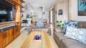 A modern living room with a large flat-screen TV, wooden cabinets, a leather sofa, and a coffee table. - The Tygervalley Escape (Cape Town)